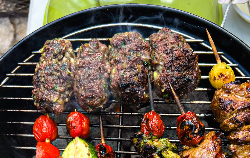 Hot Charcoal grill with four kebabs made of ground meat, chopped herbs, spices. Next to them on the grill are skewers with other grilled meat and grape tomatoes.